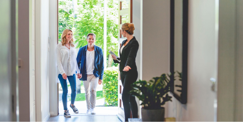 A couple entering a home with a realtor holding the door open.